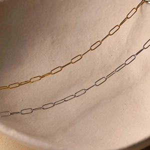 Minimalist 14k gold and silver paperclip link chain necklaces on a textured ceramic surface
