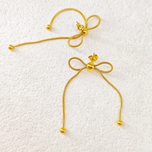 Detail of elegant gold bowknot earrings featuring long snake chain tassels and bead ends