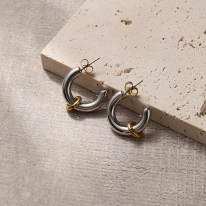 Detailed view of C-shaped silver and gold hoop earrings on natural stone surface