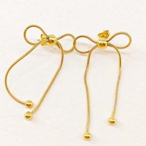 Detail of gold bow earrings featuring sleek snake chains and decorative metallic spheres