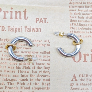Detailed macro shot of silver C-shaped earrings with gold ring accents on a paper background