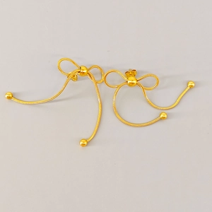 Detailed macro view of gold bow-shaped earrings with long snake chain tassels and metal beads