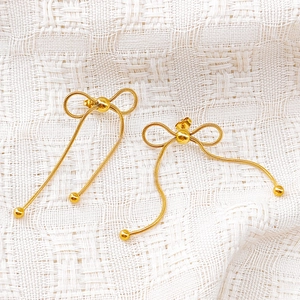 Detailed close-up of golden bow tassel earrings with sleek snake chain texture on white fabric