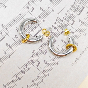 Macro detail of two-tone C-shaped hoop earrings on vintage musical sheet paper background