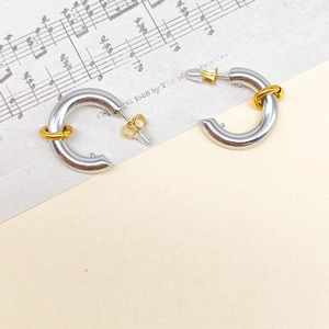 Macro detail of silver C-shaped tube earrings with gold ring accents on vintage music sheet