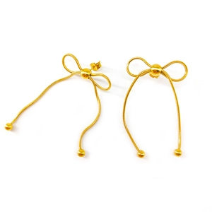 Macro detail of gold bow-shaped long tassel earrings featuring delicate snake chain design