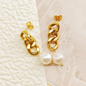 Détail de boucles d'oreilles chaînes dorées avec perles baroques sur fond texturé