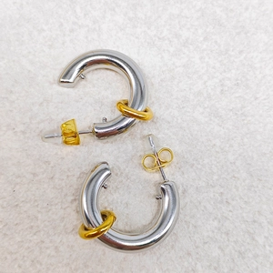 Detail view of C-shaped silver earrings with gold accent rings on textured background
