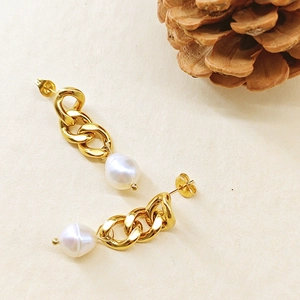 Détail de boucles d'oreilles chaîne dorées avec perles gouttes sur fond beige