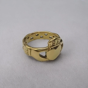 Détail d'une bague Claddagh dorée montrant des mains tenant un cœur couronné avec anneau ajouré