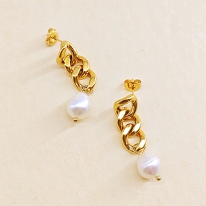 Détail macro de boucles d'oreilles chaînes dorées avec perles baroques blanches sur papier