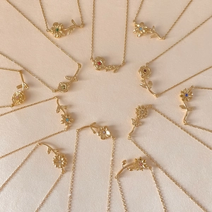 Colliers fleurs dorées avec zircons colorés disposés en cercle sur fond beige