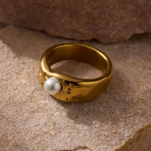 Baroque irregular molten gold ring with round pearl inlay on a natural rock surface