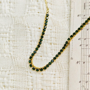 Macro detail of gold-plated tennis chain with emerald green zircon stones and claw setting