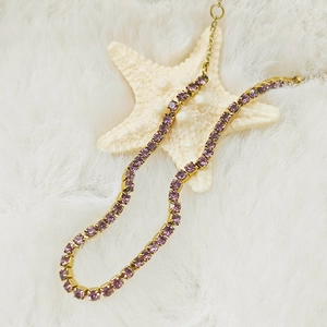 Detailed shot of a gold-plated tennis chain with lavender zircons on white faux fur