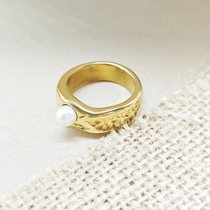 Detail of a wide gold ring with a glossy finish featuring a white baroque pearl accent