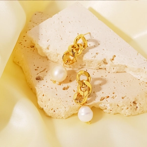 Boucles d'oreilles chaîne dorée avec grosses perles blanches sur une pierre texturée