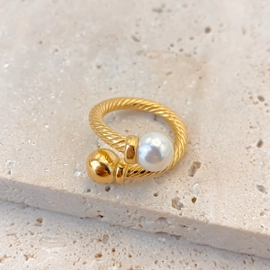 Macro view of gold twisted cable ring featuring a lustrous pearl and polished metal bead