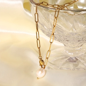 Close-up of gold paperclip link necklace with a white teardrop pearl on glass