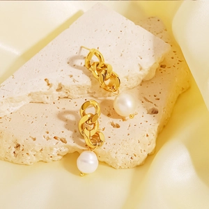 Élégantes boucles d'oreilles chaînes dorées avec perles blanches sur fond de pierre