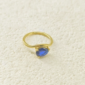 Détail macro d'une bague goutte dorée avec zircon bleu taille poire sur fond de textile blanc