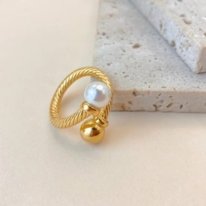 Macro detail of twisted gold-plated ring band with pearl and bead asymmetrical ends