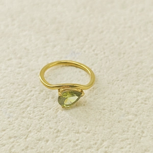 Gros plan sur un zircon vert en forme de poire sur une bague dorée ondulée