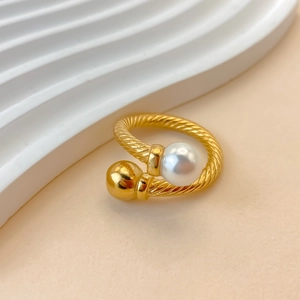 Macro shot of twisted gold-plated ring featuring a white pearl and smooth golden sphere
