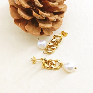Boucles d'oreilles chaîne dorée avec perles baroques sur surface beige texturée