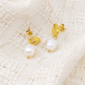 Détail des boucles d'oreilles conque dorée avec perles baroques sur tissu tressé