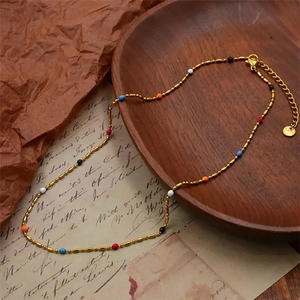 Detail of gold stainless steel necklace with colorful enamel beads on vintage paper