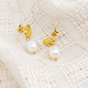 Détail de boucles d'oreilles conque dorée avec perles d'eau douce sur tissu