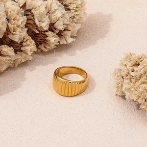 Detailed view of wide gold-plated ribbed croissant ring on a textured beige surface