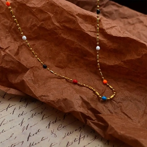 Macro detail of gold beaded chain with colorful enamel dots on vintage paper background