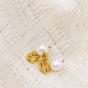 Détail des boucles d'oreilles coquillage doré avec perles sur tissu texturé