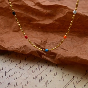 Golden stainless steel necklace with colorful rainbow enamel beads on vintage paper background