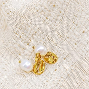 Détail des boucles d'oreilles coquillage doré et perle blanche sur tissu texturé