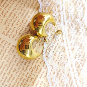Close-up of classic 18K gold-plated C-shaped hoop earrings on vintage newsprint