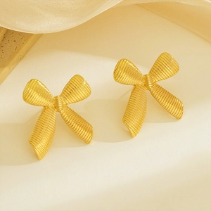 18k gold plated bow stud earrings with brushed texture surface on a stone display