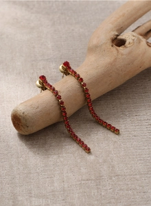 Détail de boucles d'oreilles pendantes dorées avec zircons rouges sur une branche
