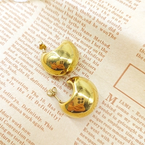 Polished 18K gold C-shape hoop earrings displayed on vintage newspaper background