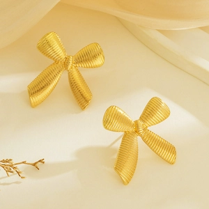 Detailed close-up of gold bow earrings with textured stripes on warm fabric background