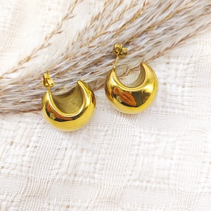 Detailed view of chunky 18K gold plated C-shaped hoop earrings on white textured fabric