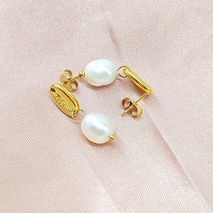 Détail des boucles d'oreilles perles baroques avec monture dorée sur tissu en soie rose