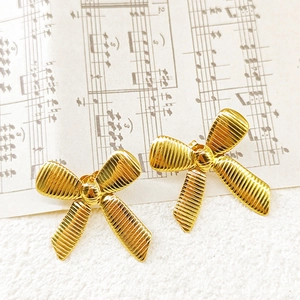 Close-up of gold bow earrings with textured finish on vintage sheet music background