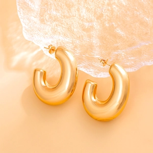 Detail of chunky gold hoop earrings with a mirror-polished finish on a neutral surface