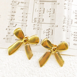 Detail shot of golden bow earrings featuring a textured striped surface on retro sheet music