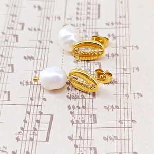 Vue détaillée des boucles d'oreilles coquillage doré et perles sur papier à musique