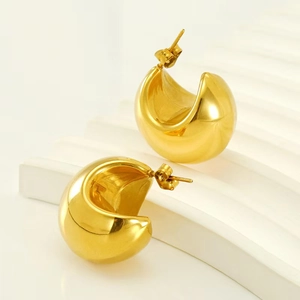 Close-up of chunky gold C-shaped hoop earrings on white display stand with elegant lighting