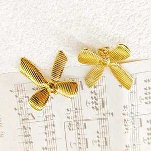 Macro view of gold-plated 18k bow earrings featuring vertical textured metal pleats